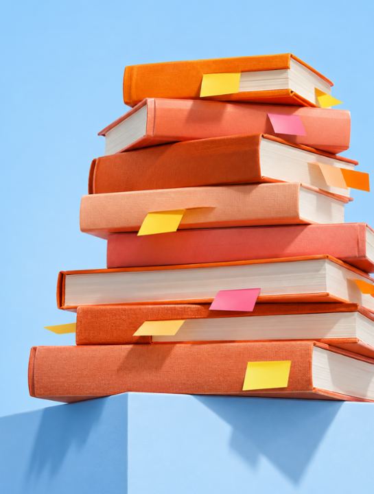 Pilha de livros laranja com marcadores amarelos sobre fundo azul.